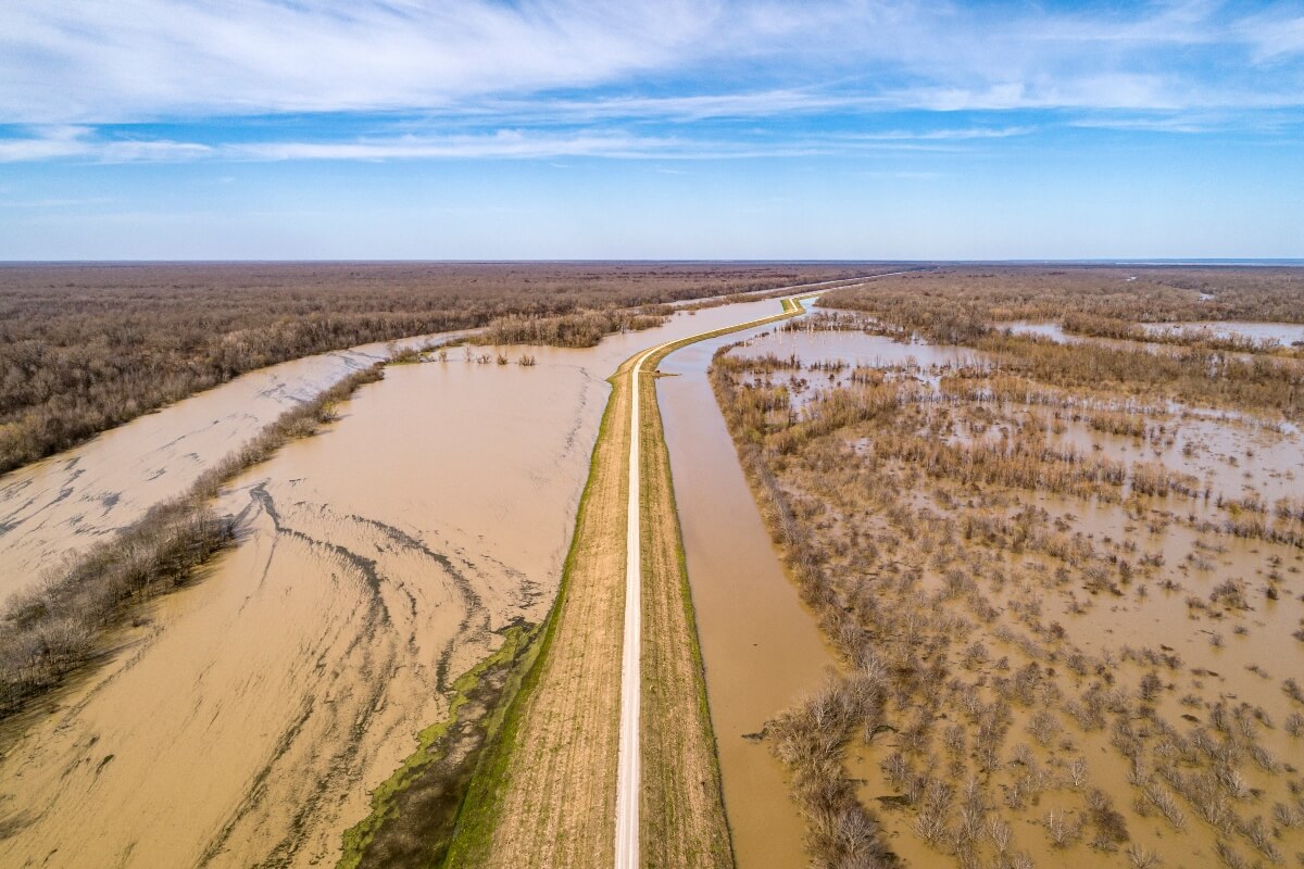 Aerial view of a long road through a flooded landscape, with water on both sides under a partly cloudy sky